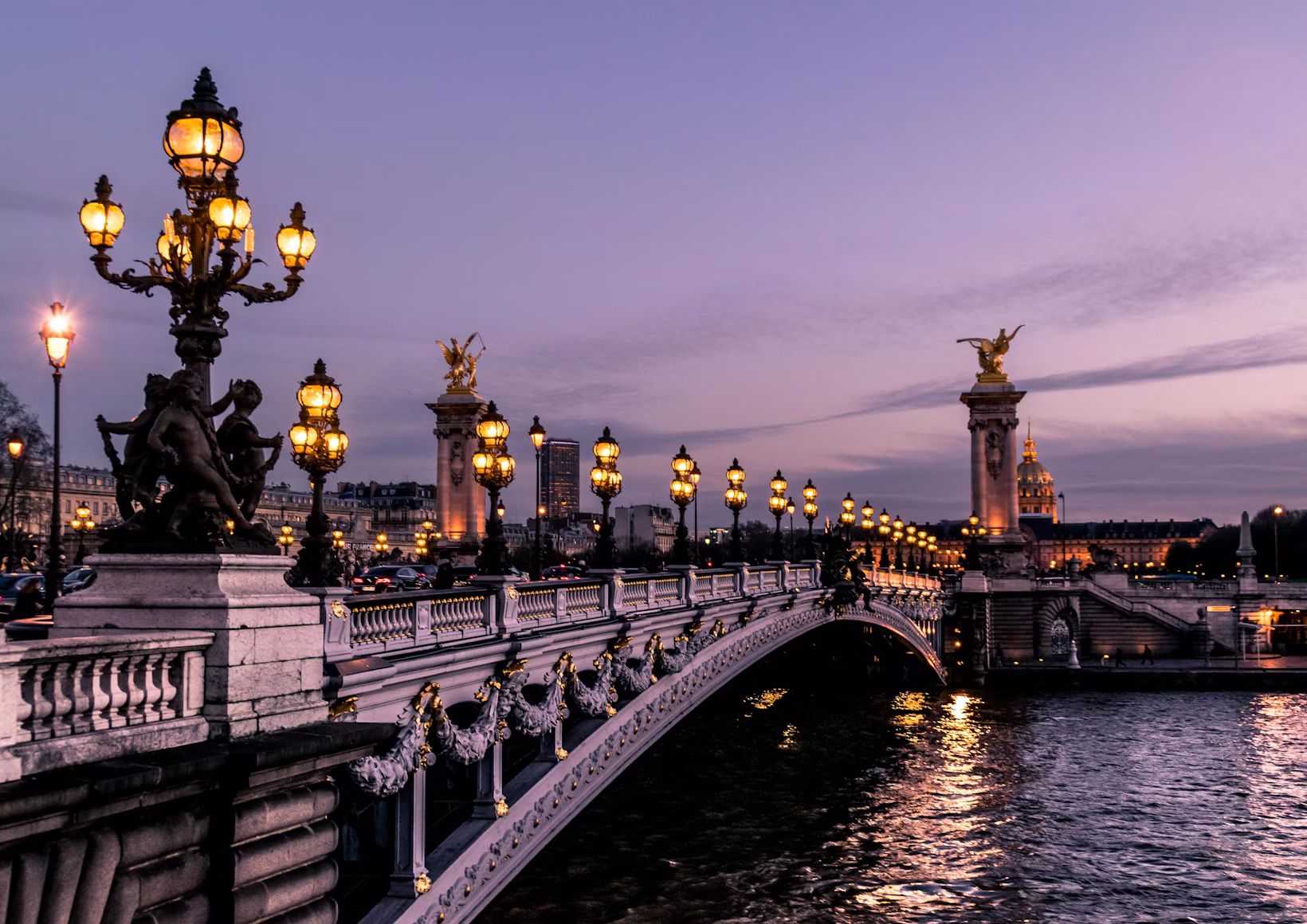 A gilded Paris bridge lit at dusk with the river running beneath it