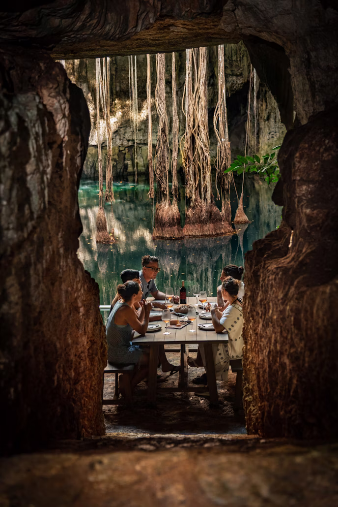 A long table set for a group inside a cavern, lit by lanterns, with water beyond
