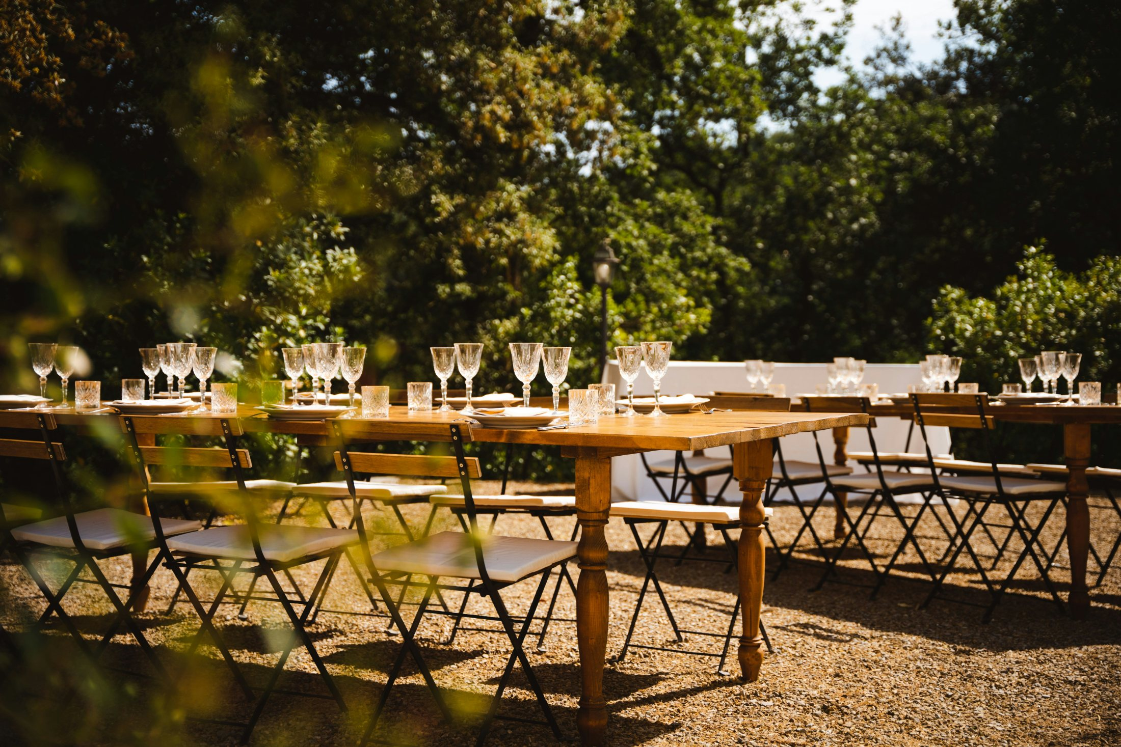 A long outdoor dinner table set with wine glasses beneath the trees